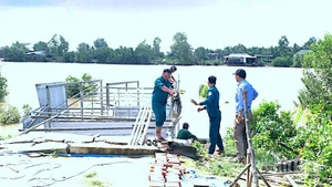 Lực lượng chức năng địa phương hỗ trợ tháo dỡ nhà bà Bích vốn bị nhấn chìm xuống sông sau vụ sạt lở.