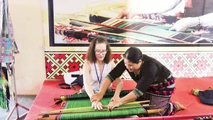 Nghệ nhân H’Bình giới thiệu cách dệt thổ cẩm dân tộc Mạ cho du khách nước ngoài đến tham quan tổ hợp tác.