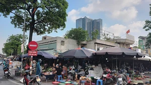 Các quầy, sạp bên trong chợ Ngã Tư Sở bị bỏ không, nhưng nhiều người dân lại tràn ra vỉa hè để bán hàng. (Ảnh VĂN HỌC) 