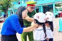 Giáo viên và cán bộ Công an hướng dẫn học sinh đội mũ bảo hiểm đúng cách.