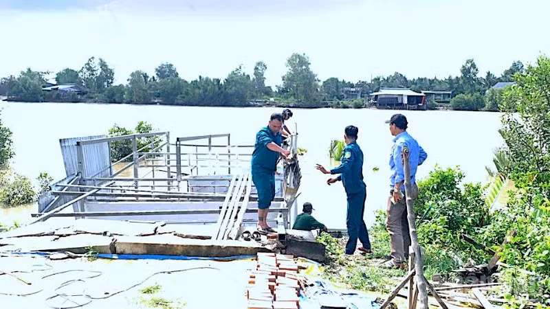 Lực lượng chức năng địa phương hỗ trợ tháo dỡ nhà bà Bích vốn bị nhấn chìm xuống sông sau vụ sạt lở.