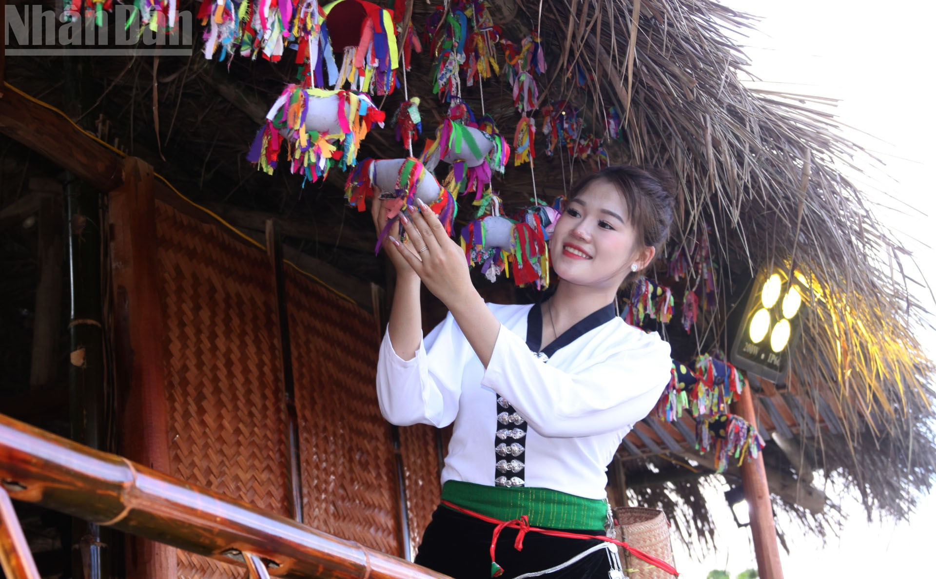 អ្នកទេសចរម្នាក់ឈរក្បែរផ្លែឈើព្យួរនៅមុខរានហាលនៃផ្ទះថ្ម ដែលបង្ហាញពីលំហវប្បធម៌របស់ជនជាតិឡាវ-ខ្មែរ។ ndo_tl_6.jpg
