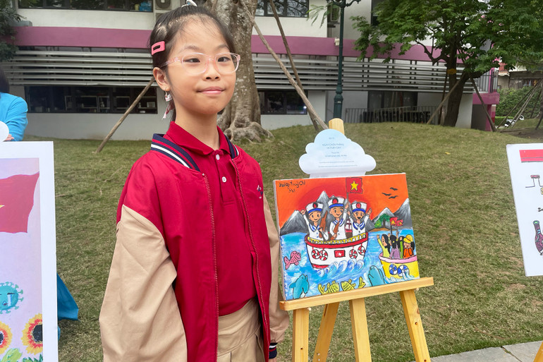 Em Hoàng Thùy Chi (10 tuổi, bị khuyết tật bẩm sinh mắt khi một bên không thể nhìn) bên cạnh tác phẩm "Ngày chiến thắng".