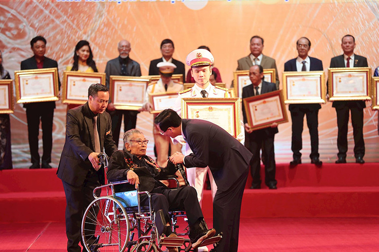 Nghệ sĩ Nhân dân Hoàng Quân Tạo đi xe lăn lên sân khấu nhận phong tặng danh hiệu năm 2024. Nghệ sĩ Nhân dân Hoàng Quân Tạo đi xe lăn lên sân khấu nhận phong tặng danh hiệu năm 2024.