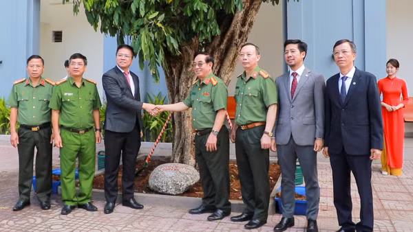 Lãnh đạo nhà trường và đại diện đoàn công tác chụp ảnh bên cây nhãn trồng lưu niệm. 