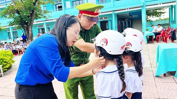 Giáo viên và cán bộ Công an hướng dẫn học sinh đội mũ bảo hiểm đúng cách.