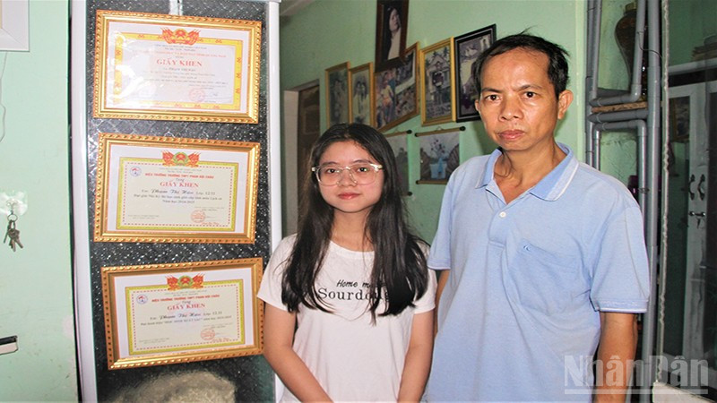 Em Phạm Thị Hậu và cậu ruột Ngô Thanh Đoàn đứng bên các thành tích học của em Hậu.