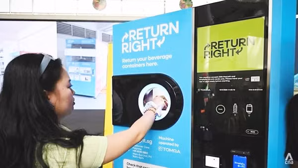 Một người tiêu dùng đặt chai nhựa rỗng vào máy thu gom. Ảnh: CNA