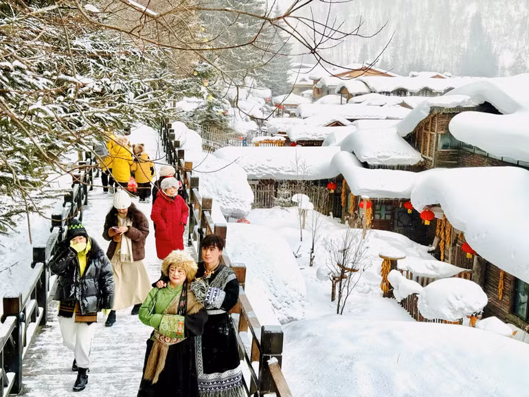 Du khách trong trang phục truyền thống check-in bên những mái nhà phủ đầy tuyết trắng.