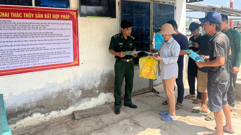 Cán bộ Ðồn Biên phòng Hàm Luông phát tờ rơi tuyên truyền cho ngư dân tại cảng cá Ba Tri (tỉnh Bến Tre) về chống khai thác thủy sản bất hợp pháp. (Ảnh HOÀNG TRUNG)