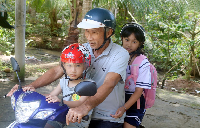 Ông Nguyễn Văn Tấn, ấp Định Bình, xã Long Thới, huyện Tiểu Cần, tỉnh Trà Vinh đưa các cháu ngoại đến trường.