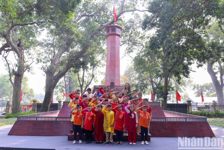 Cô và trò trường Tiểu học Tràng An (quận Hoàn Kiếm) thực hiện nghi thức chào cờ tại triển lãm tương tác Cột cờ Hà Nội tại trụ sở Báo Nhân Dân. Ảnh: Thế Đại