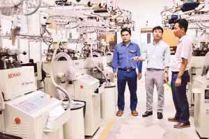 Anh Nguyễn Thanh Bình (đứng giữa), Giám đốc Công ty TNHH Begen, giới thiệu về dây chuyền sản xuất bít-tất xuất khẩu.