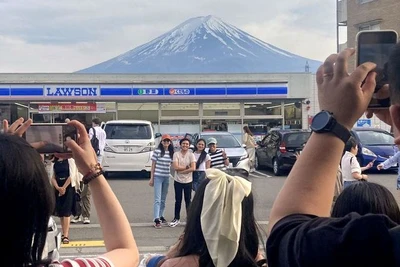 Khách du lịch chụp ảnh với khung cảnh núi Phú Sĩ phía sau cửa hàng tiện lợi Lawson ở thị trấn Fujikawaguchiko, tỉnh Yamanashi, Nhật Bản, ngày 28/4/2024. (Ảnh: Reuters/Kyodo) 