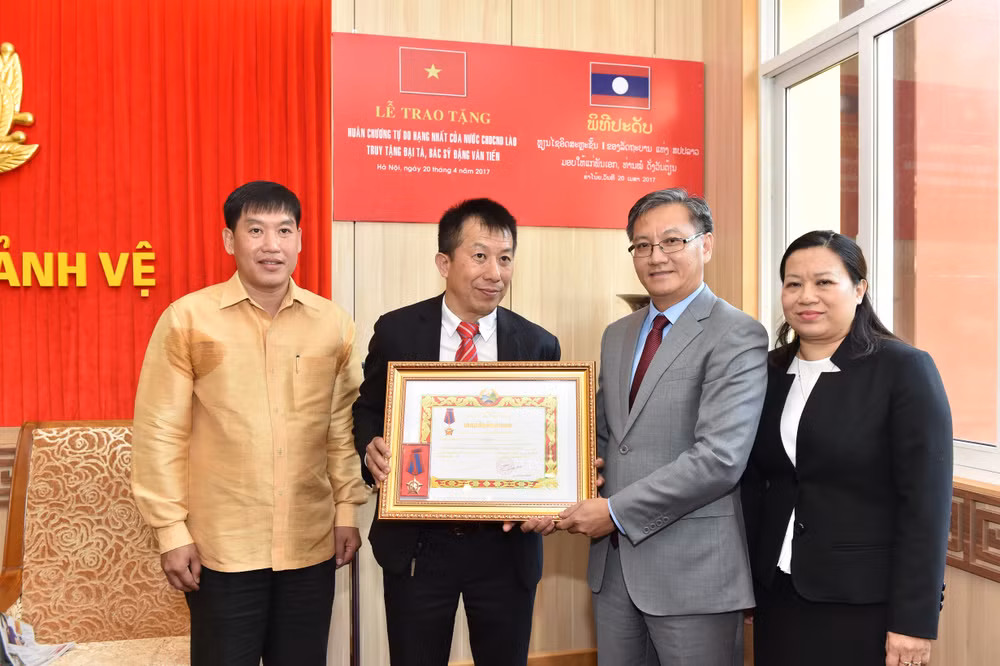 Đồng chí Thong Sa-vẳn Phôm-vi-hản, Đại sứ đặc mệnh toàn quyền nước CHDCND Lào tại Việt Nam trao tặng Huân chương cho gia đình Đại tá, bác sĩ Đặng Văn Tiến.