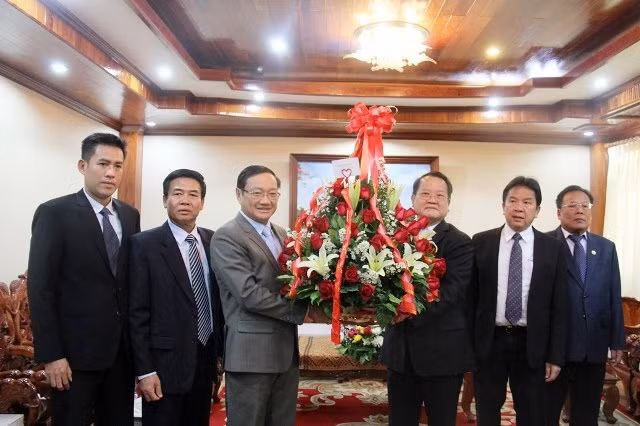 Đại sứ Nguyễn Bá Hùng (thứ ba từ trái sang) chuyển lẵng hoa của Tổng Bí thư Nguyễn Phú Trọng chúc mừng 63 năm Ngày thành lập Đảng NDCM Lào.