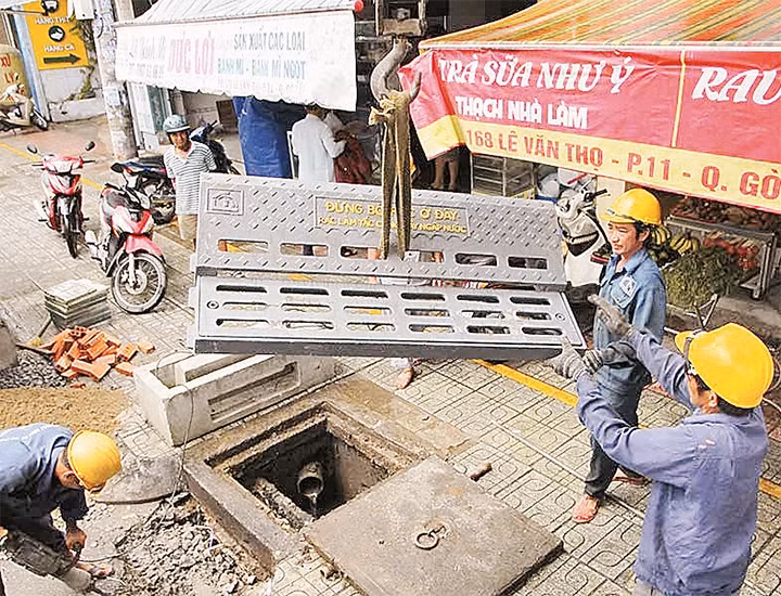Công nhân lắp đặt nắp ngăn rác trên miệng hố ga. 