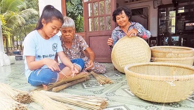 Bà Trần Thị Đo (thứ hai từ trái qua), xã Thái Mỹ, huyện Củ Chi hướng dẫn cháu nghề đan lát truyền thống của địa phương.