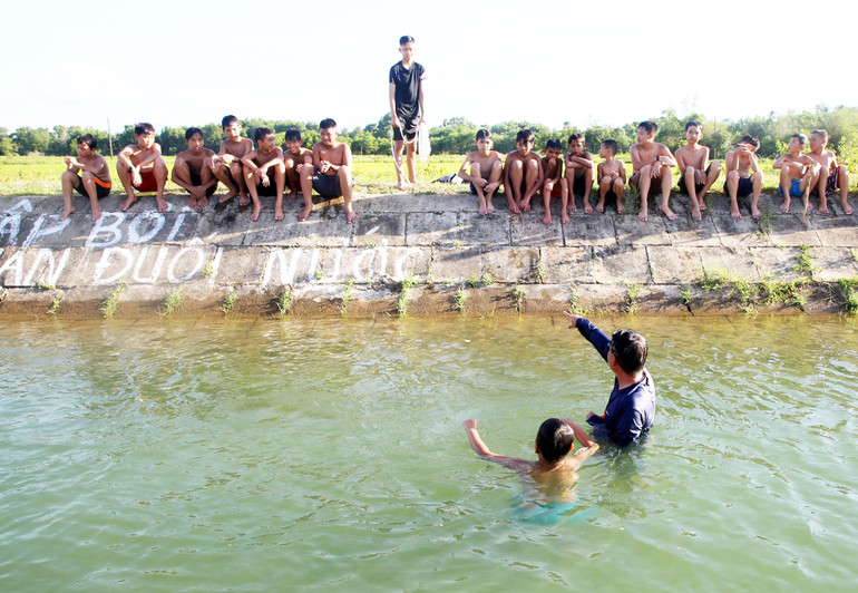 Nhiều học sinh ngồi trên bờ kênh đợi đến lớp học của mình.