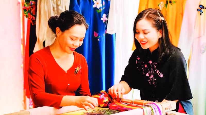 Nghệ nhân Nguyễn Thị Hằng (bên trái) giới thiệu kỹ thuật thêu trên lụa. (Ảnh: THÀNH NAM)