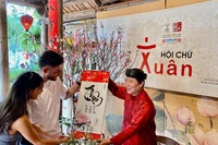 Một "thầy đồ" hiện đại trao bức thư pháp chữ quốc ngữ tặng du khách nước ngoài trong ngày đầu Xuân tại Văn Miếu-Quốc Tử Giám (Hà Nội). 