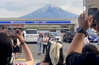 Khách du lịch chụp ảnh với khung cảnh núi Phú Sĩ phía sau cửa hàng tiện lợi Lawson ở thị trấn Fujikawaguchiko, tỉnh Yamanashi, Nhật Bản, ngày 28/4/2024. (Ảnh: Reuters/Kyodo) 