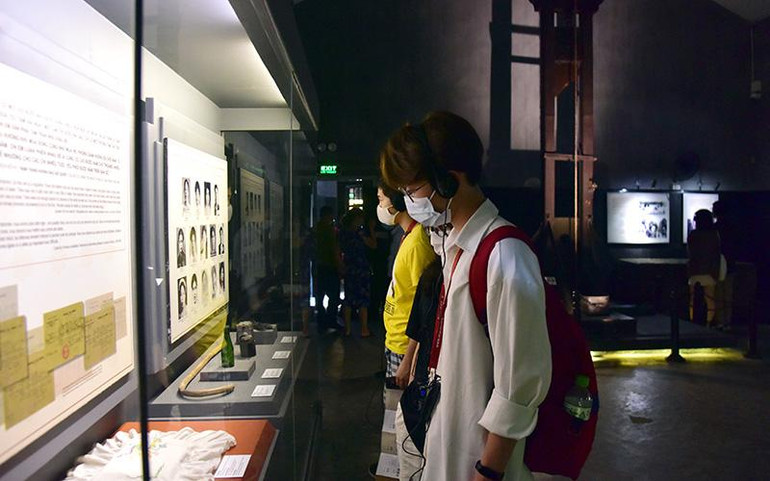 Du khách sử dụng bộ đàm thuyết minh tự động khi tham quan di tích Nhà tù Hỏa Lò, Hà Nội. (Ảnh HÀ THU)