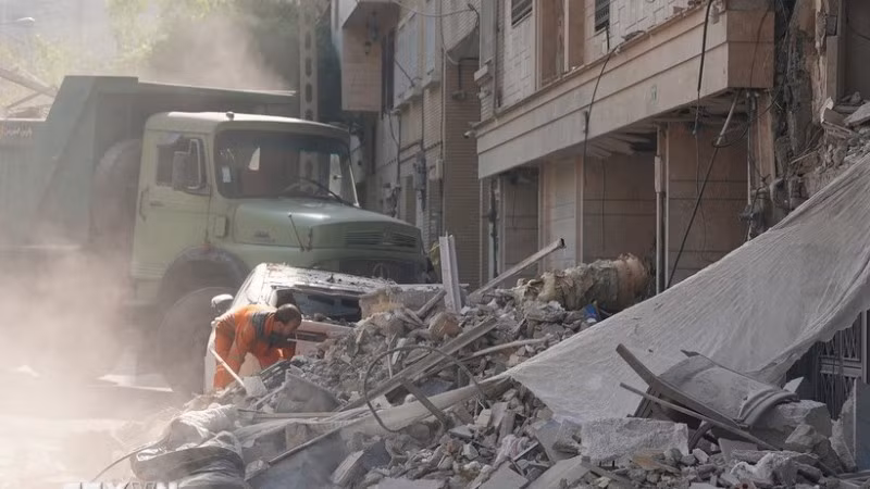 Nhân viên cứu hộ dọn đống đổ nát của tòa nhà bị sập tại Tehran, Iran sau các cuộc không kích của Israel. (Ảnh: THX/TTXVN)