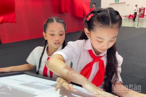 Em Đỗ Phương Linh cùng bạn khám phá sách tương tác mapping tại Triển lãm “95 năm Cờ Đảng soi đường”.