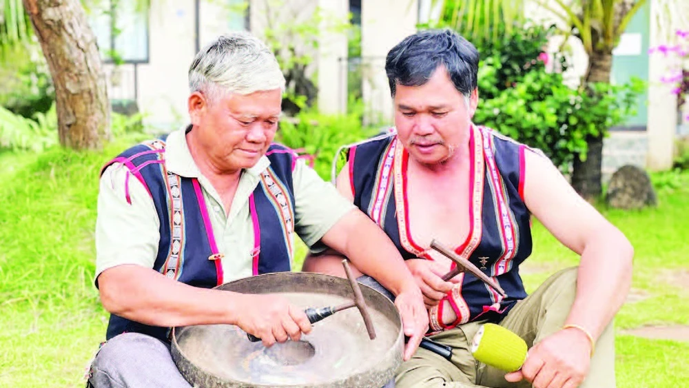 Nghệ nhân Ưu tú Đinh Dôch (bên trái) hướng dẫn kỹ thuật chỉnh chiêng cho học viên. (Ảnh LAM NGUYÊN)