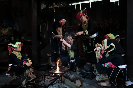 Bà Bàn Minh Toan cùng các phụ nữ Dao Lù Gang quây quần bên bếp lửa thực hiện công đoạn sơn đầu, trong không gian sinh hoạt đậm chất cộng đồng.