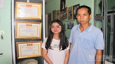 Em Phạm Thị Hậu và cậu ruột Ngô Thanh Đoàn đứng bên các thành tích học của em Hậu.