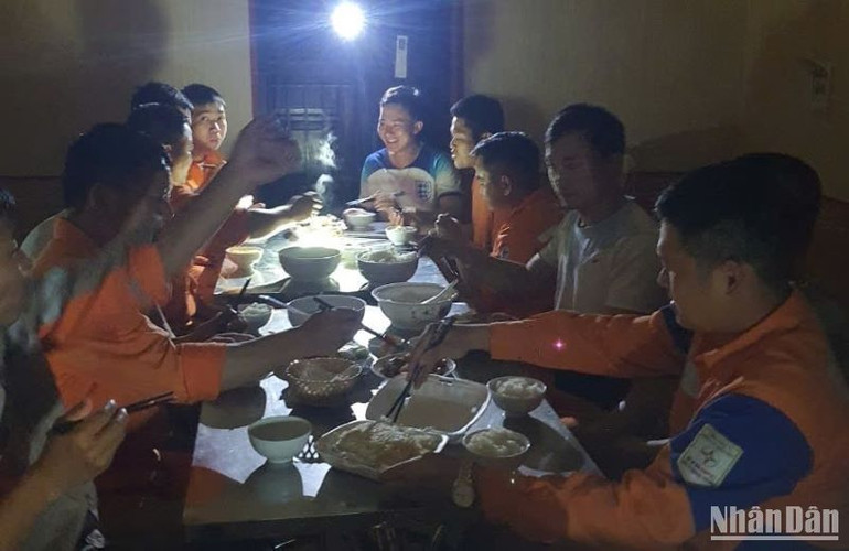Công nhân Điện lực Thái Thụy tranh thủ ăn tối trong ánh sáng le lói của đèn tích điện để tiếp tục ca làm việc ban đêm.