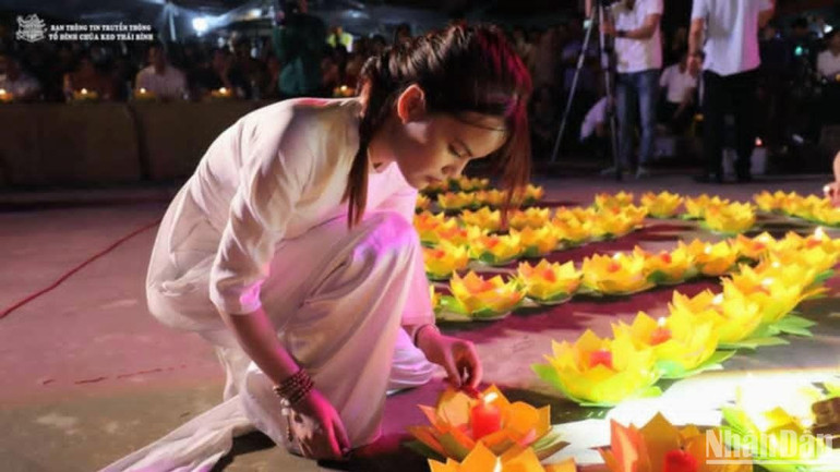 Một thiếu nữ trong tà áo dài đang nghiêm ngắn sắp xếp, chỉnh sửa những cánh hoa đăng.