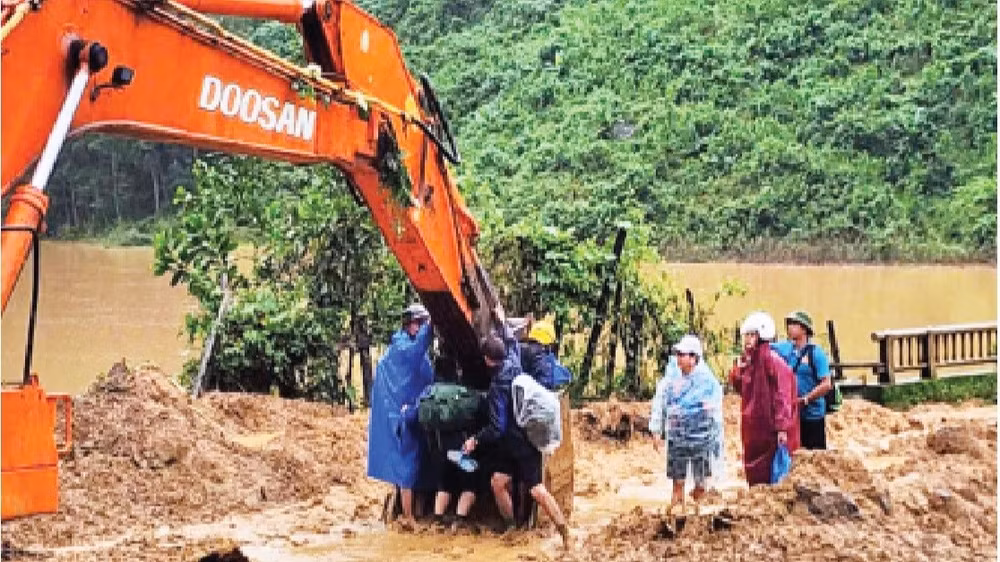 Các thầy, cô giáo ở xã Phước Chánh phải ngồi trên gàu của xe múc để vượt qua chỗ sạt lở vào trường học. (Ảnh: ANH QUÂN)