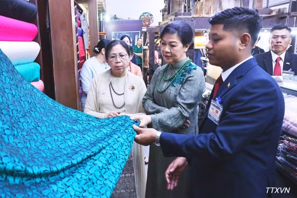 Phu nhân Ngô Phương Ly và Phu nhân Kyu Kyu Hla tham quan khu trưng bày sản phẩm lụa truyền thống và giới thiệu các sản phẩm đặc sắc của làng nghề Vạn Phúc. (Ảnh: TTXVN)