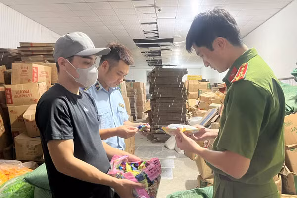 Lực lượng chức năng kiểm tra địa điểm sản xuất kinh doanh bánh, kẹo, nước uống do Nguyễn Quang Đạt (đeo khẩu trang) làm chủ. (Ảnh: Công an Hà Nội)