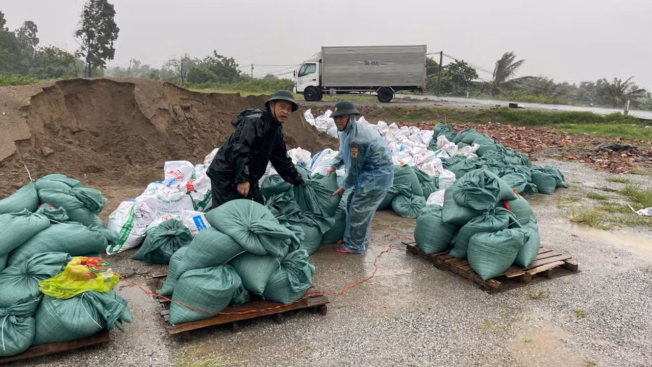 Lực lượng hộ đê đang cho cát vào các bao tải để phòng gia cố đê kè, trong khi mưa bắt đầu to hơn. (Ảnh: MAI TÚ)
