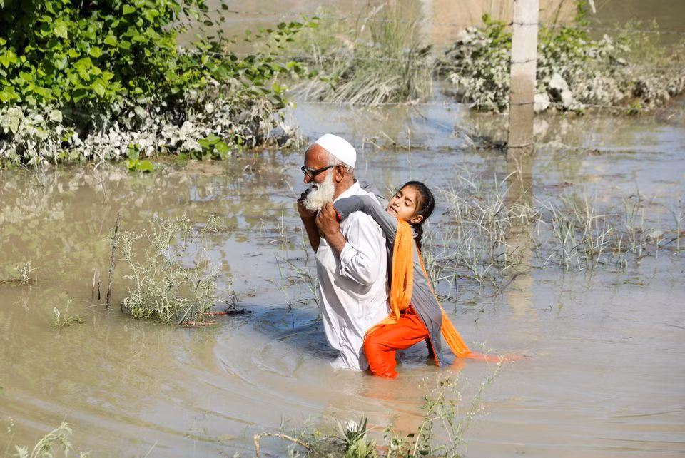 Ông cõng cháu vượt qua đoạn đường bị ngập tại khu vực Charsadda, ngày 28/8. (Ảnh: Reuters)