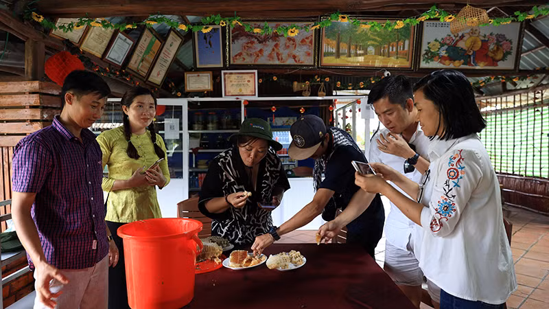 Anh Phạm Duy Khanh, chủ cơ sở du lịch cộng đồng Mười Ngọt (ngoài cùng bên trái), hướng dẫn khách thưởng thức ong non khai thác từ rừng U Minh Hạ.