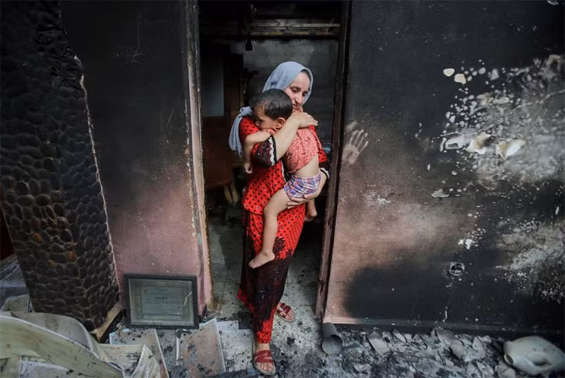 Cô Souhila Belkati cùng con đứng trong ngôi nhà bị đám cháy rừng tại Bejaia, Algeria, thiêu trụi. (Ảnh: Reuters)