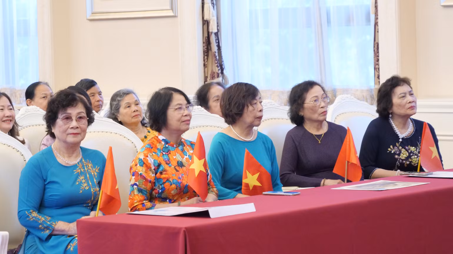 Các bác, các chị trong trang phục áo dài truyền thống cầm cờ Tổ quốc.