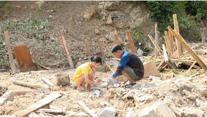 Em Moong Thị Phương Thảo và bố nhặt lại những cuốn sách còn có thể dùng được trong ngôi nhà bị lũ cuốn trôi.
