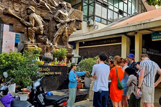 Du khách nước ngoài tìm hiểu về ý nghĩa của bức phù điêu “Hà Nội mùa đông năm 1946” trước cổng chợ Đồng Xuân, Hà Nội. (Ảnh: T.LINH)