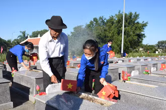 Ông Nguyễn Bá Sanh hướng dẫn các em đoàn viên thanh niên của xã Hòa Phong cắm cờ Tổ quốc lên phần mộ từng liệt sĩ.