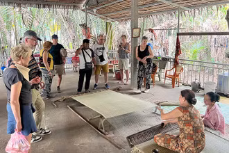Khách du lịch nước ngoài theo dõi công đoạn dệt chiếu tại xã Nhơn Thạnh (thành phố Bến Tre, tỉnh Bến Tre).