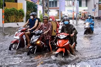 Người dân vất vả di chuyển trên đoạn ngập sâu ở đường Quốc Hương (thành phố Thủ Đức). (Ảnh: Hồng Giang/TTXVN)