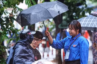 Tình nguyện viên hỗ trợ đón thí sinh vào điểm thi trong cơn mưa sáng 9/1 (Ảnh: TUẤN ANH/TTXVN)