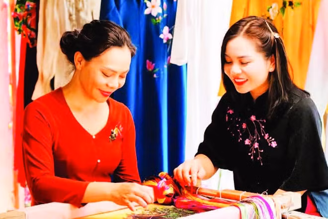 Nghệ nhân Nguyễn Thị Hằng (bên trái) giới thiệu kỹ thuật thêu trên lụa. (Ảnh: THÀNH NAM)