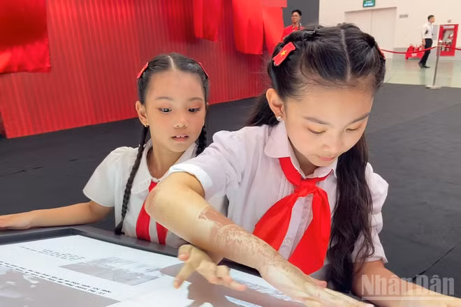 Em Đỗ Phương Linh cùng bạn khám phá sách tương tác mapping tại Triển lãm “95 năm Cờ Đảng soi đường”.